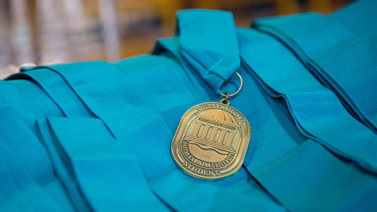 Graduation stoles are displayed with a medallion recognizing outstanding student achievement, representing honors‑level academic distinction.